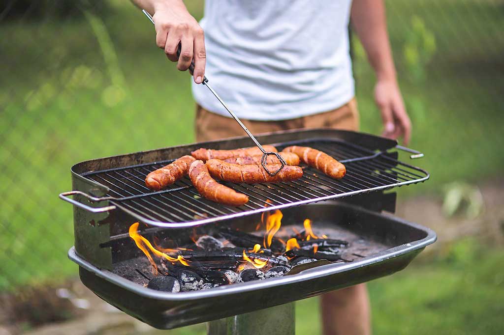 Ein Mann grillt Würste auf dem offenen Holzkohlegrill