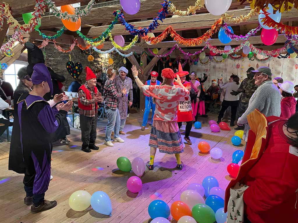 Verkleidete Menschen tanzen bei einer Faschingsfeier in einem bunt mit Girlanden und Luftballons geschmückten Saal